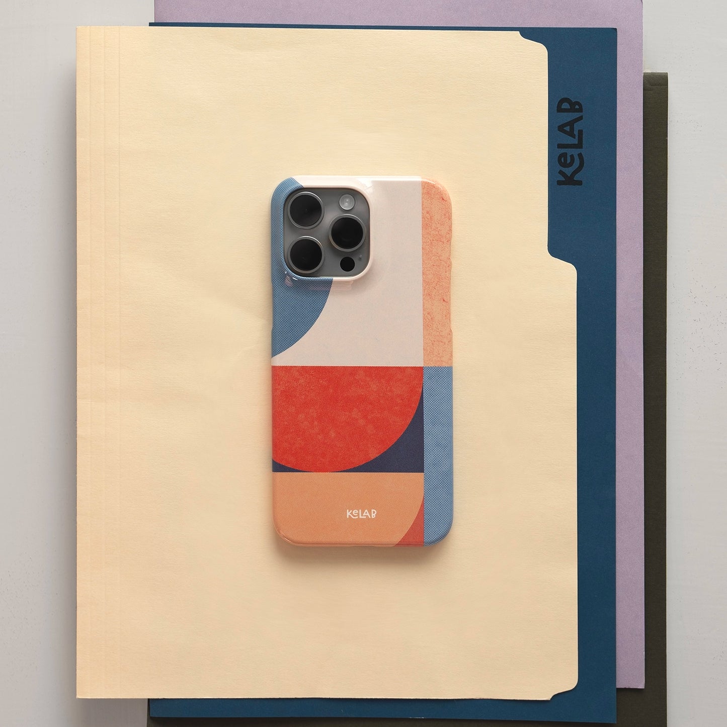 Modern art phone case with red, navy, and cream geometric design placed on folders. Aesthetic and functional iPhone case by KELAB.