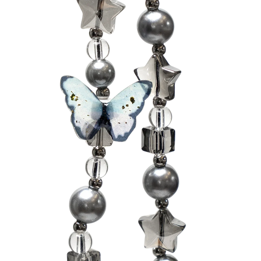 Close-up of Moonshade Phone Charm by KELAB showing detailed blue butterfly, pearl beads, and star-shaped accents in a monochrome palette.