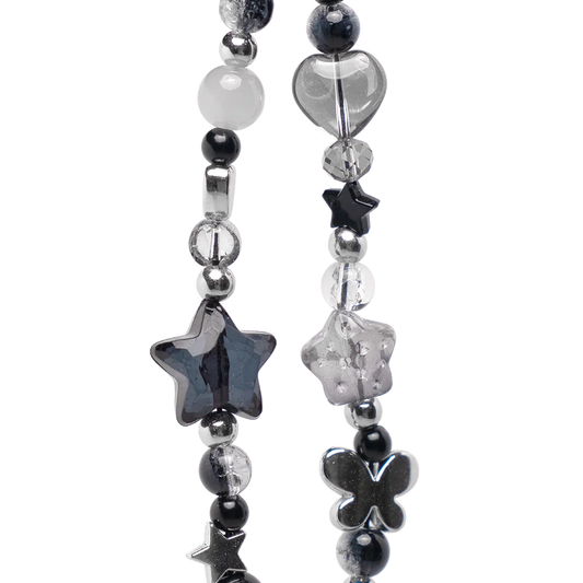 Close-up of chrome phone charm showing star, heart, and butterfly beads in black and crystal tones. Edgy Y2K aesthetic for iPhone accessories.