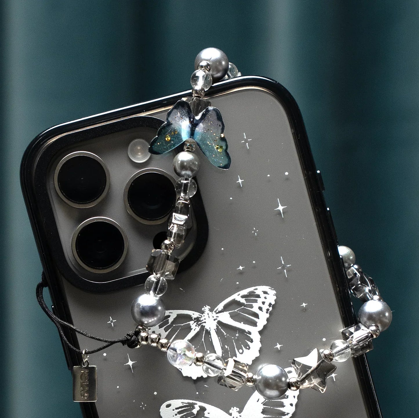 Detailed view of Moonshade Phone Charm by KELAB on a smartphone, highlighting the butterfly charm and pearl-studded strap for soft glam appeal.