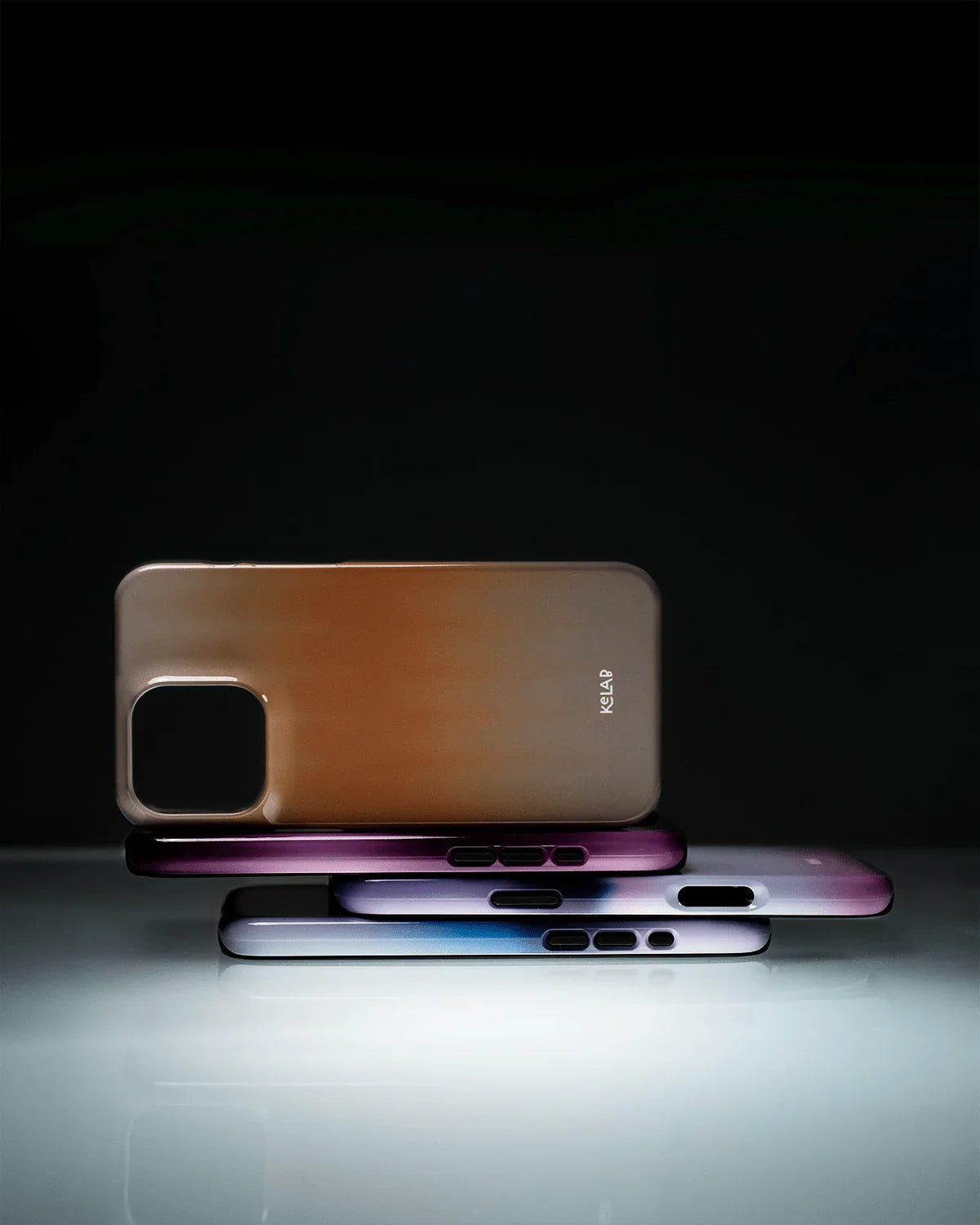 Artistic display of KELAB’s Tinted Veil Series phone cases in gradient colors, highlighting the minimalist orange case with sunset tones.