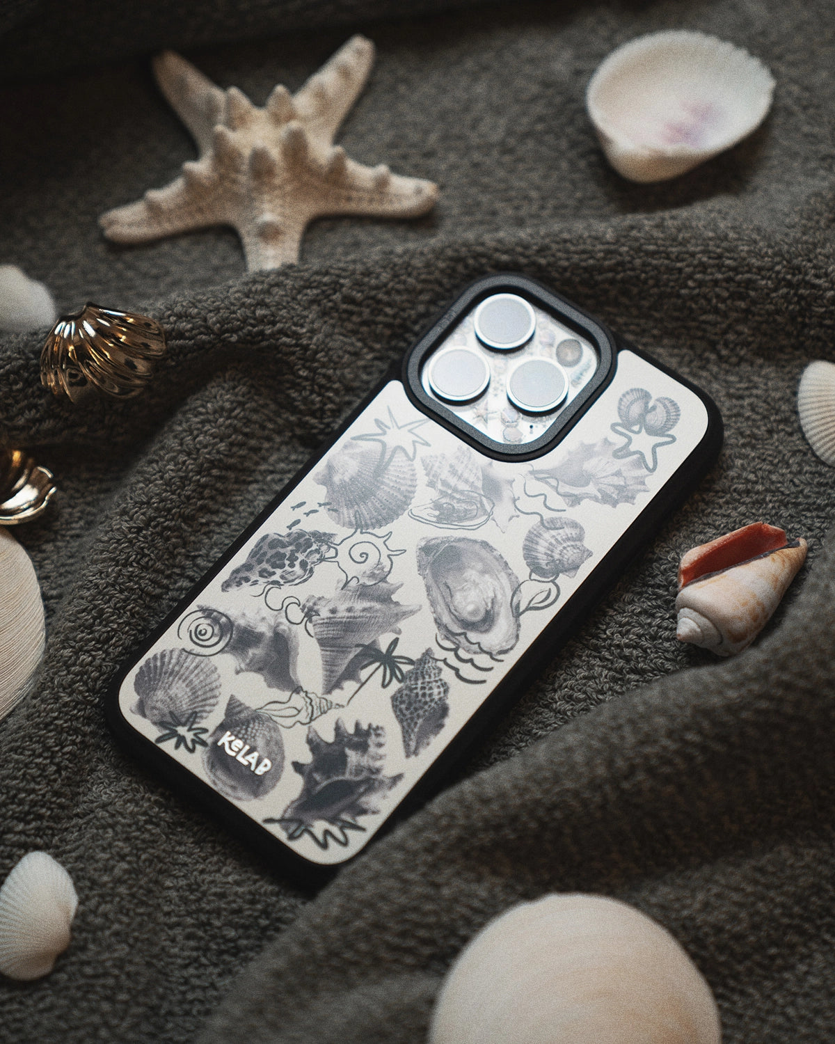 KELAB iPhone case with sea-themed design on a textured surface with shells and a starfish.