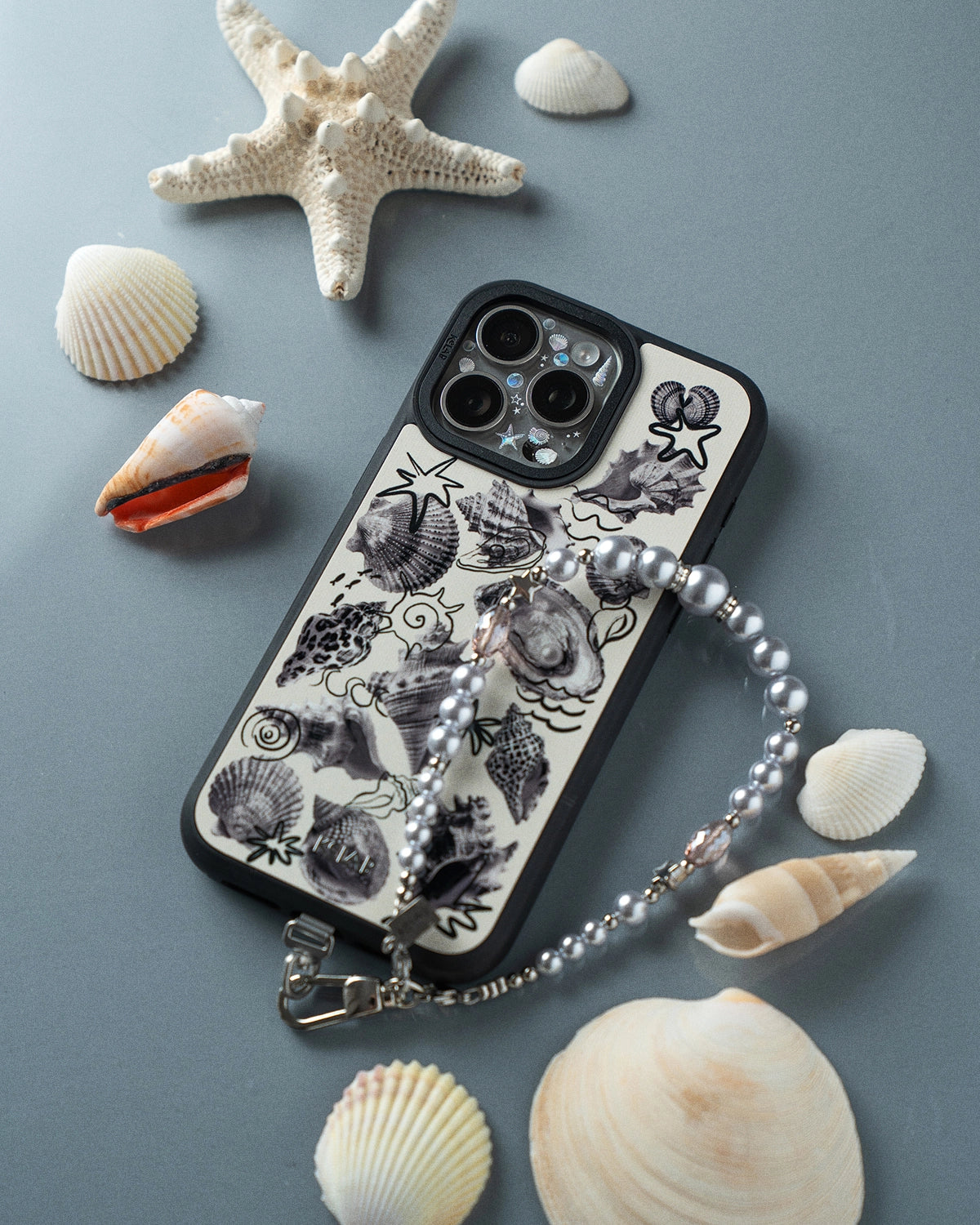 KELAB iPhone case with seashell design and chain on a light blue background with shells and a starfish.