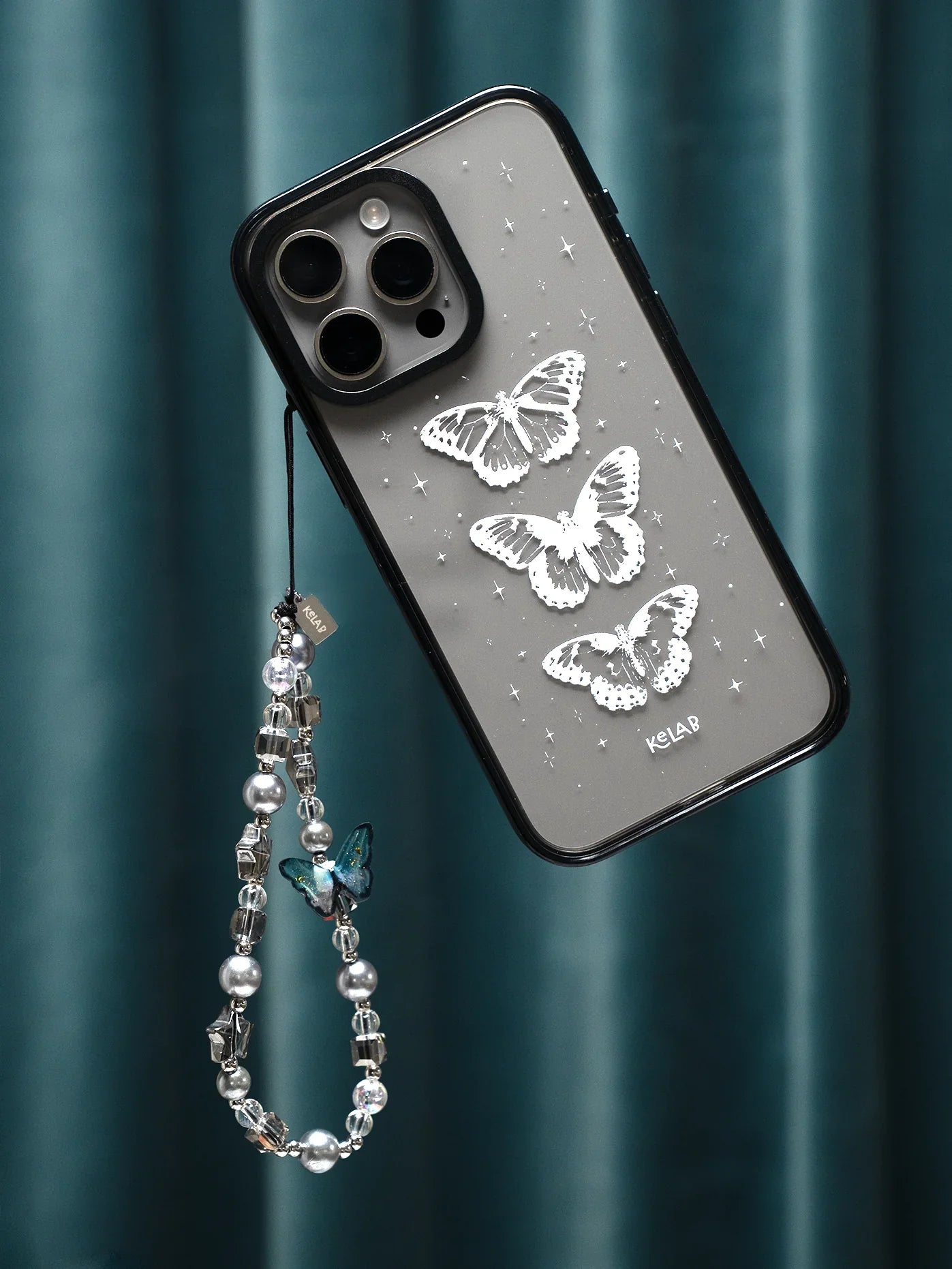 Moonshade Butterfly & Pearl Phone Charm by KELAB attached to a phone case with silver butterfly design, blending celestial and glam aesthetics.